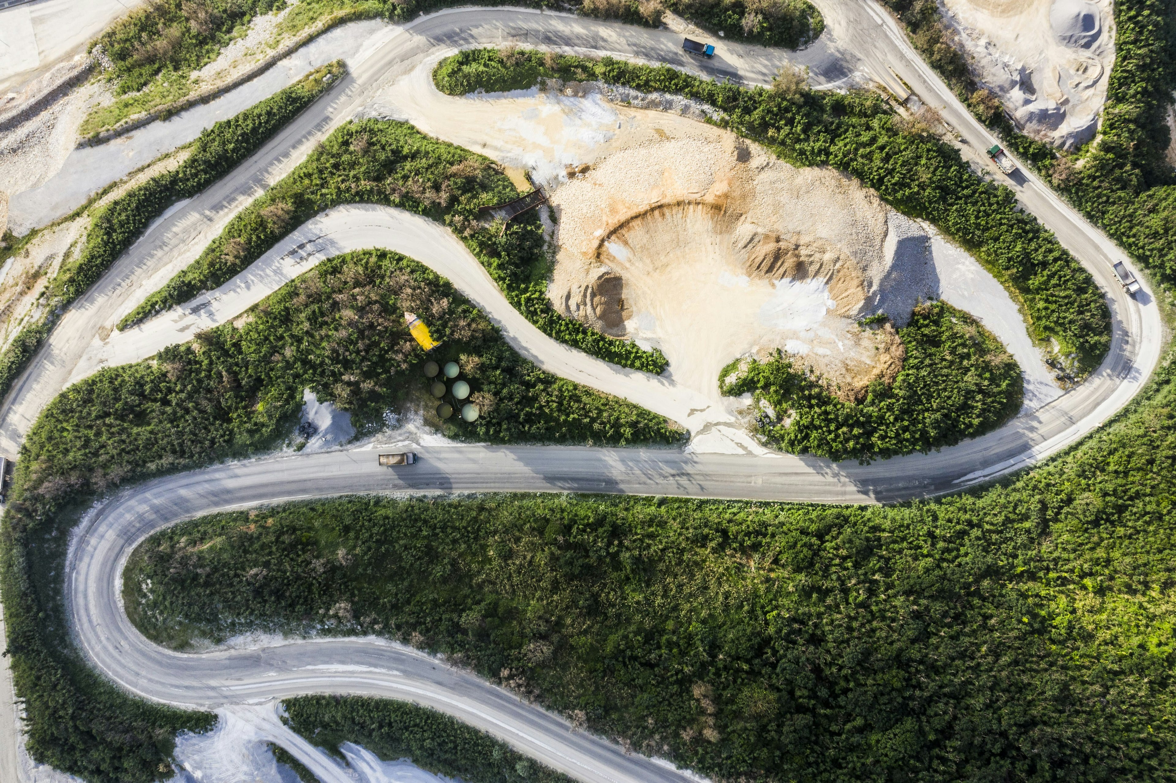 Aerial view of green mining site and roadway with trucks driving through