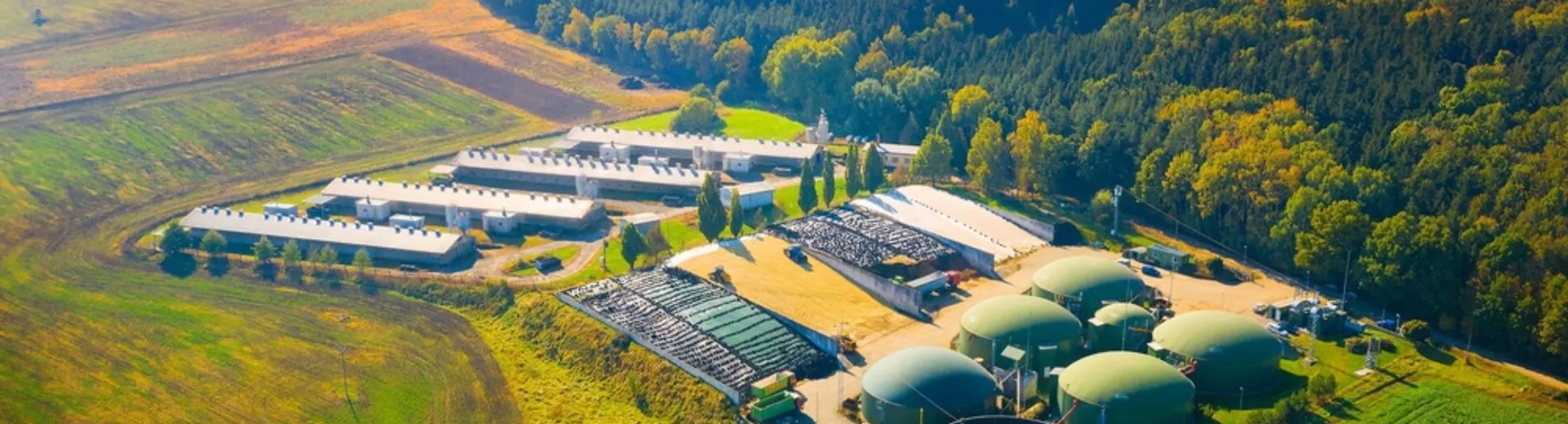 Biogas plant and farm in green fields against sunset